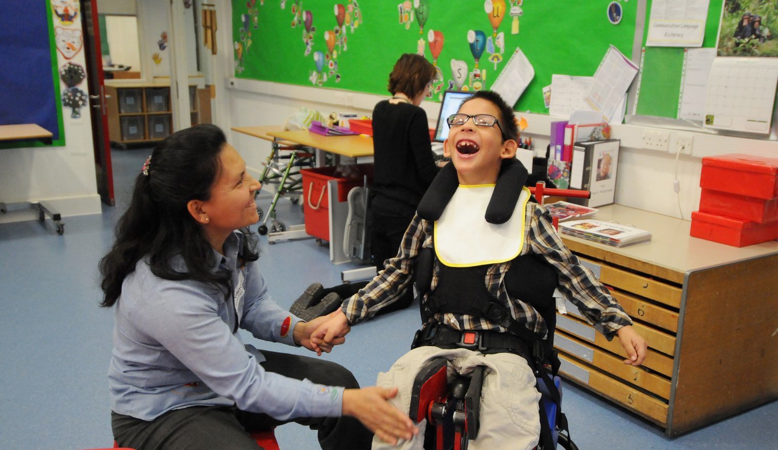 A boy with cerebral palsy smiles in our dynamic seat as his mother looks on smiling